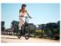 Lächelnde Frau mit Helm und leichter Kleidung fährt an einem sonnigen Tag E-Bike.