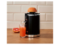 Schwarze Zitruspresse mit Grapefruit, die Saft in ein Glas auf einer Holzoberfläche presst.