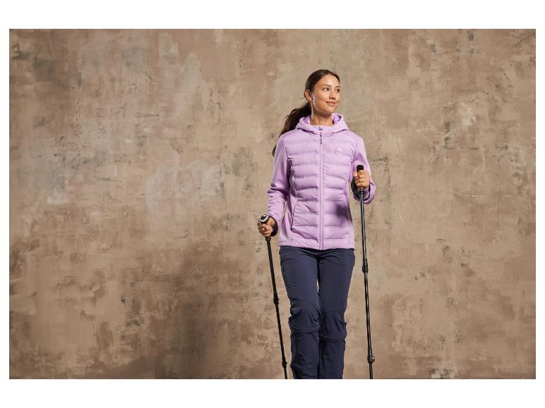 Eine Frau in einer lila Jacke mit Kapuze und Wanderstöcken.