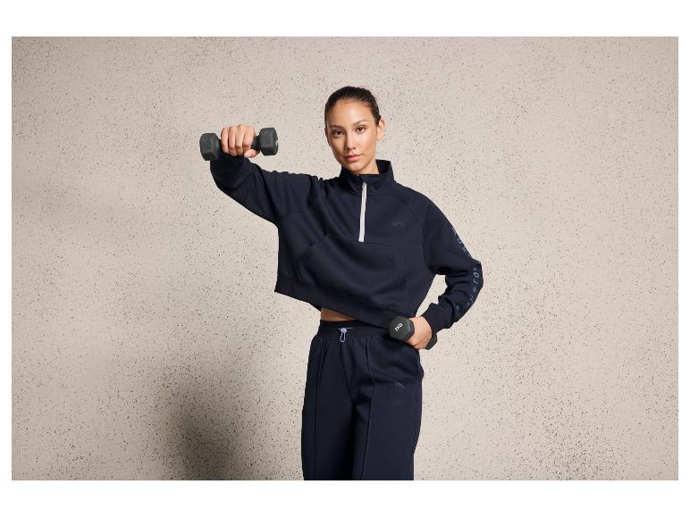 Eine Frau in einem dunkelblauen Sweatshirt und einer Hose, die während des Trainings Gewichte hebt.