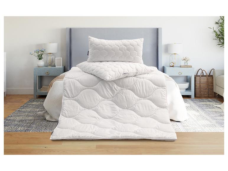 Schlafzimmer mit Bett, Nachttischen, Lampe und einem Set weißer Bettdecken und Kissen.