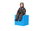 Kind in Leoparden-Overall mit Ohren, sitzend auf einem blauen Würfel.