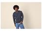 Mann in blauem Langarmshirt und Jeans, posiert vor hellem Hintergrund.