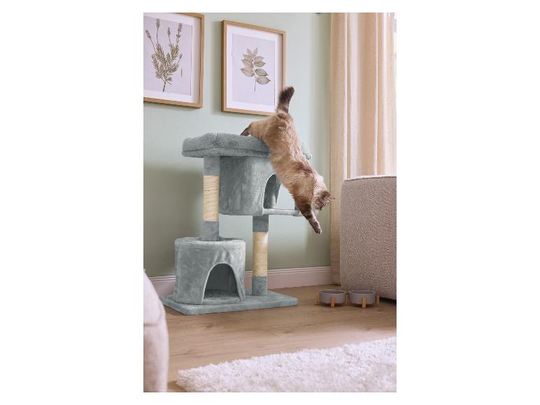 Katze springt von einem mehrstufigen Kratzbaum in einem Wohnzimmer mit Futternäpfen.