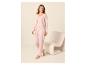 Frau in einem hellrosa Pyjama-Set mit Strickjacke und Hose, neben einem Stuhl stehend.