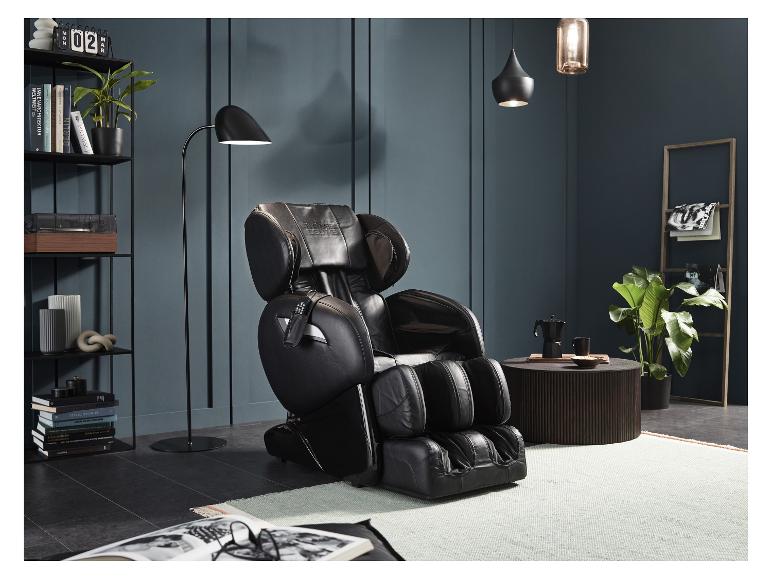 Schwarzer HOME DELUXE Massagesessel in einem modernen Wohnzimmer mit Regalen und Pflanzen.