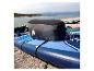Blaues Paddleboard mit grauer Sitztasche an einem Kiesstrand.