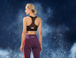 Eine Frau trägt einen schwarzen Sport-BH und lila Leggings mit rotem Streifen.