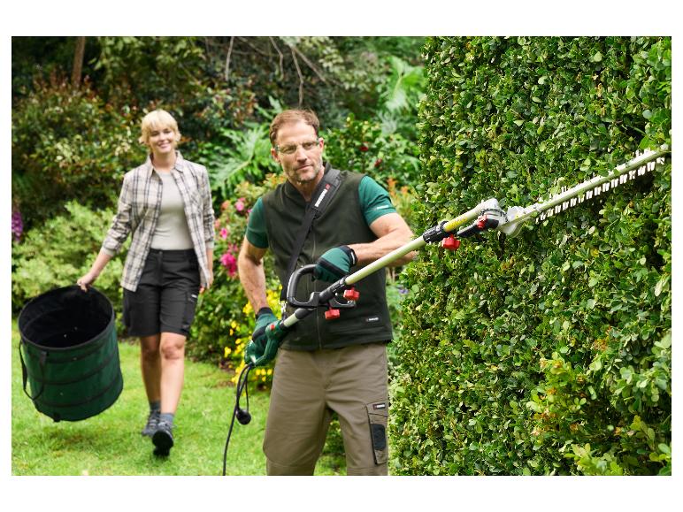 Mann schneidet Hecke mit Parkside-Trimmer, Frau trägt Gartensack.