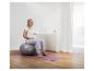 Schwangere Frau sitzt auf einem grauen Gymnastikball auf einer lila Yogamatte.