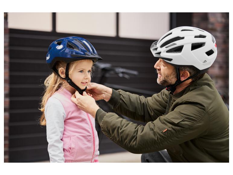 Ein Mann hilft einem Kind, einen blauen und weißen Craftig Fahrradhelm aufzusetzen.