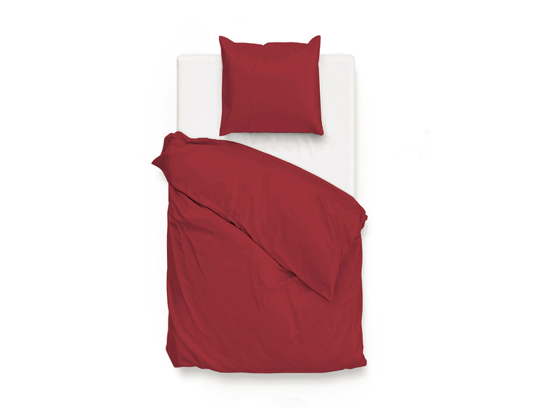 Eine rote Bettdecke und ein Kissen auf einem weißen Bett.