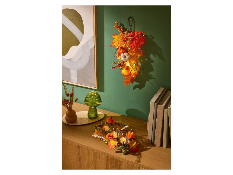 LIVARNO home Herbstdekoration mit LED-Lichtern, Kerzen und bunten Blättern.