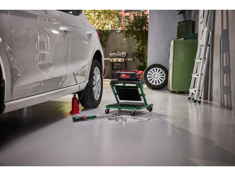 Auto auf Wagenheber mit Werkzeugen, Ladegerät und Rollwagen in der Garage.
