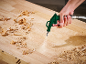 Handgeführte Druckluftpistole reinigt Holzspäne von einer Werkbank.