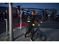 Mann in reflektierender Fahrradjacke, Helm und Handschuhen schiebt ein Fahrrad in der Dämmerung.