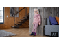 Mädchen in rosa Strickpullover, Leggings und Winterschuhen an einer Holzwand.