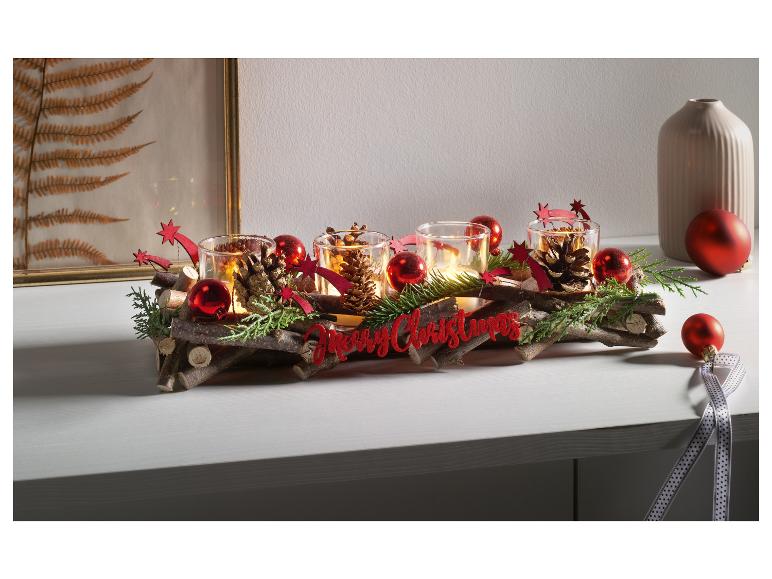 Weihnachtsdekoration mit Kerzen in Gläsern, Ästen, roten Weihnachtskugeln und einem 'Merry Christmas'-Schild.