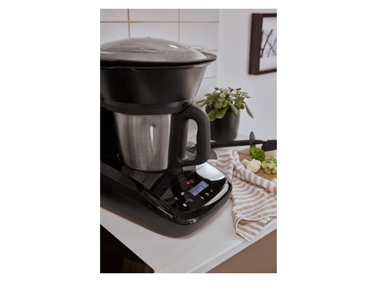 Schwarze Küchenmaschine mit Edelstahlschüssel und transparentem Deckel auf einer weißen Arbeitsplatte.