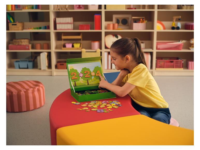 Mädchen spielt mit einem magnetischen Zahlen- und Buchstabenpuzzle an einem bunten Tisch.