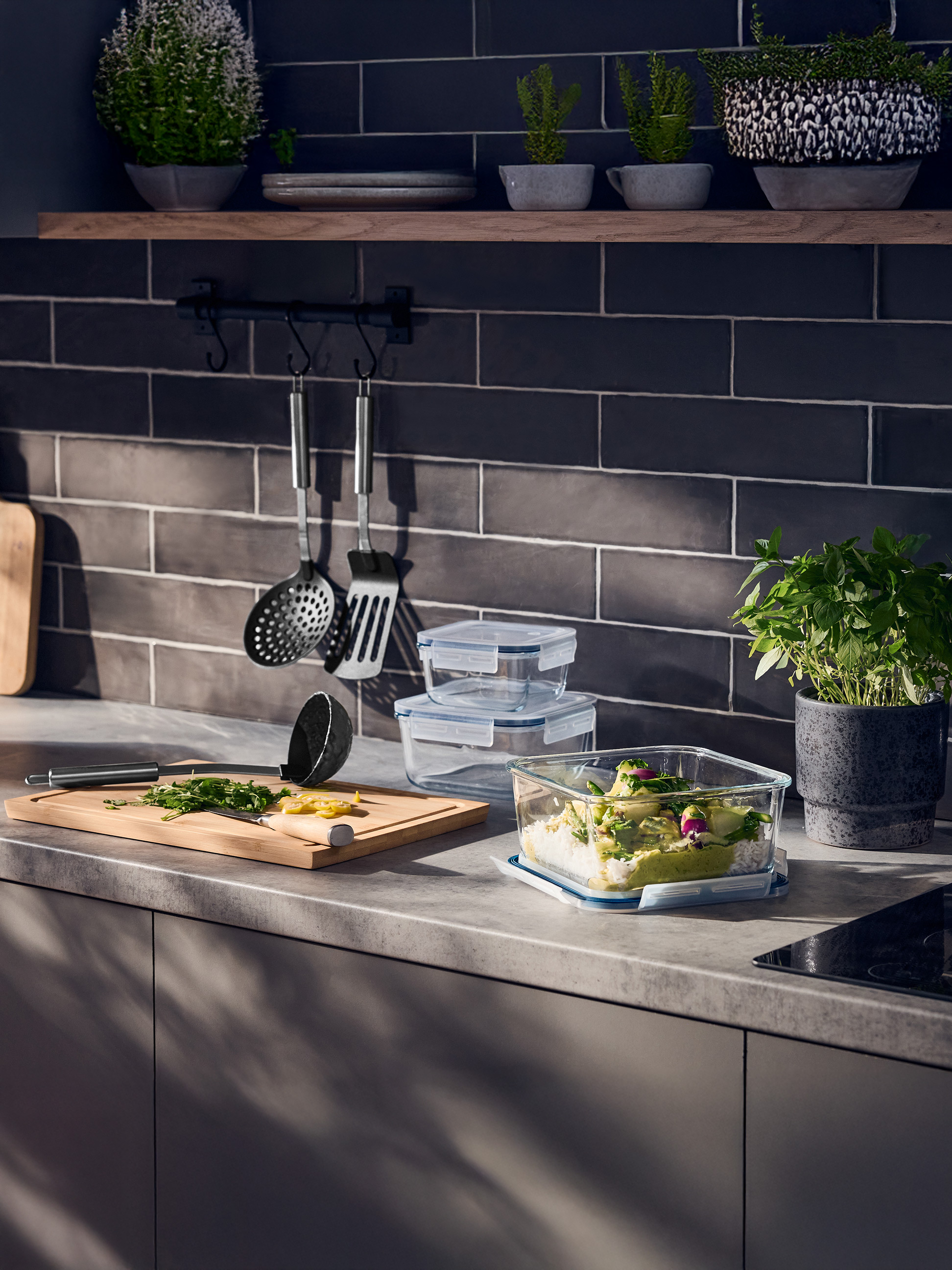 Küchenzeile mit Glas-Frischhaltedosen, Schneidebrett und Kräutern.