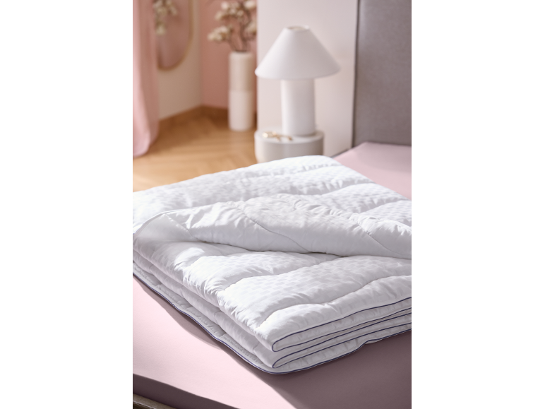 Weiße Bettdecke auf rosa Laken in einem Schlafzimmer mit Nachttischlampe.