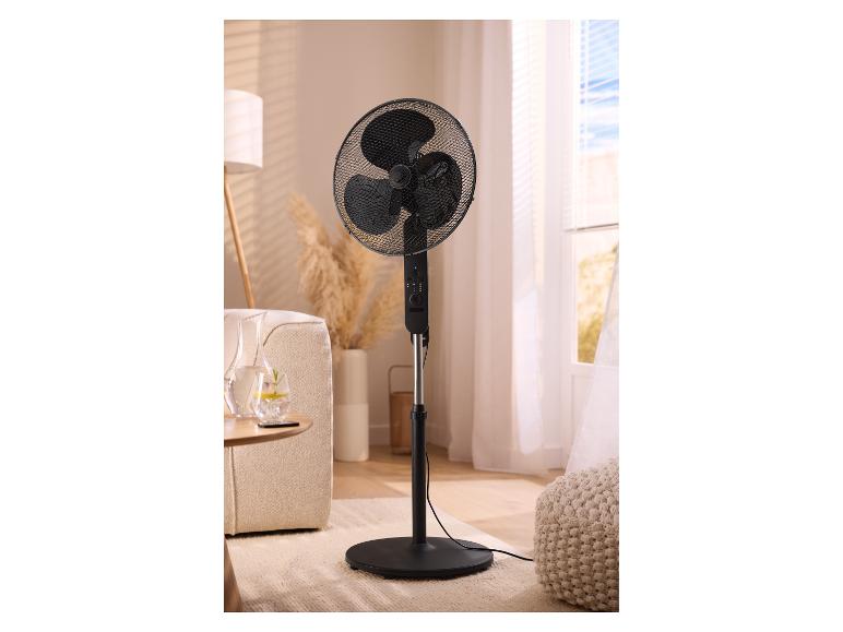 Schwarzer Standventilator in einem Wohnzimmer mit Sofa, Lampe und Fenster.