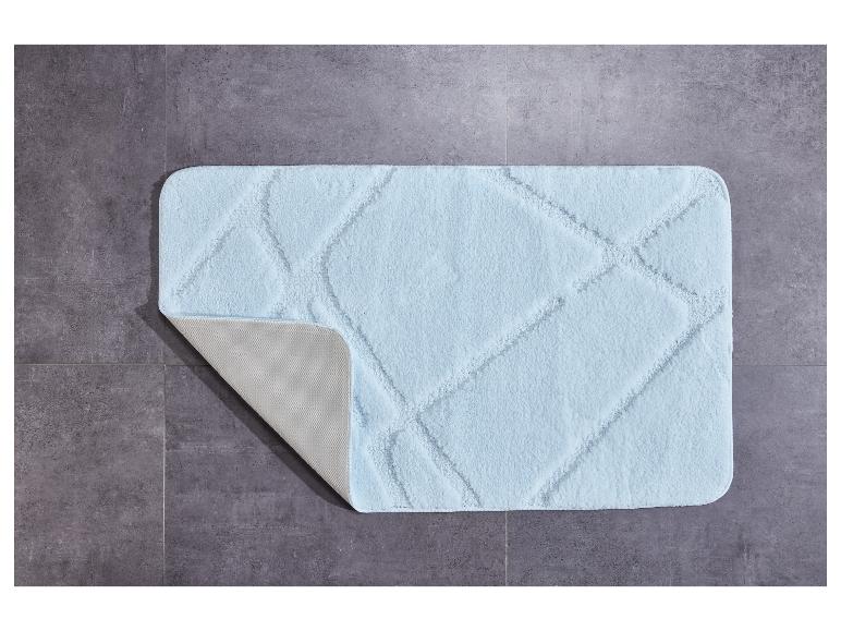 Ein hellblauer Badezimmerteppich mit Rautenmuster auf einem grauen Fliesenboden.