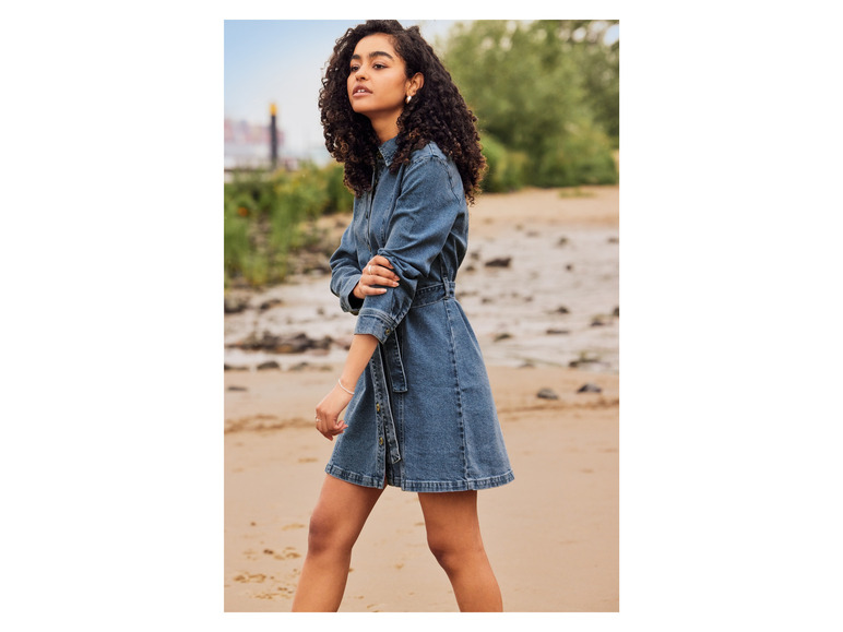 Eine Frau trägt ein Jeanskleid an einem Sandstrand.