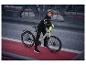 Frau in Radsportkleidung und Helm, lehnt auf beigem Fahrrad auf einer Brücke.