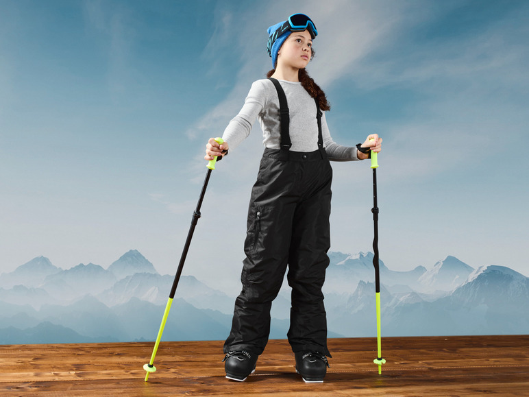 Ein Mädchen in Skikleidung mit Stöcken, bereit zum Skifahren.