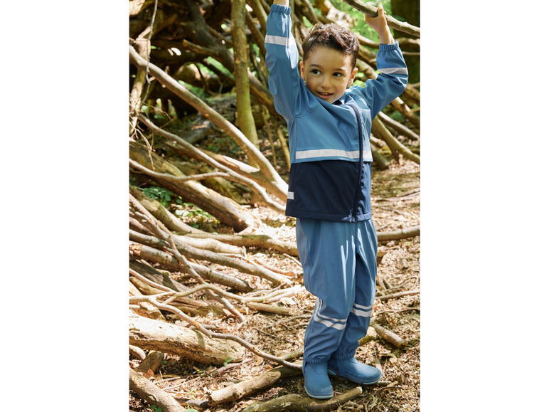 Ein Junge in einer blauen Regenjacke und Hose in einem Wald