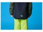 Ein Kind in einer dunkelblauen Skijacke und neongrünen Skihose.