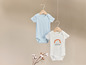 Zwei Babybodys mit kurzen Ärmeln, einer hellblau und einer weiß mit Regenbogen-Motiv.