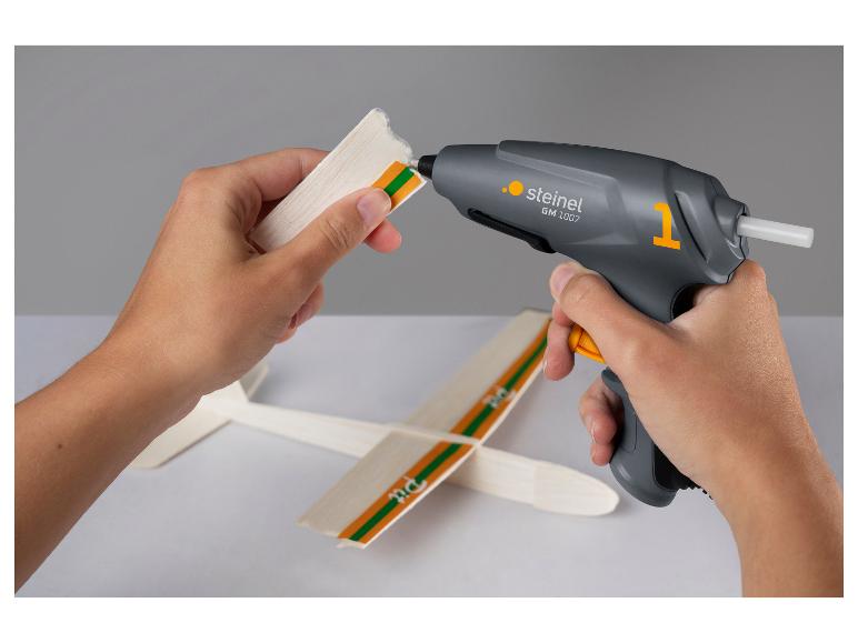 Hände verwenden eine Heißklebepistole, um ein Holzspielzeugflugzeug zusammenzubauen.