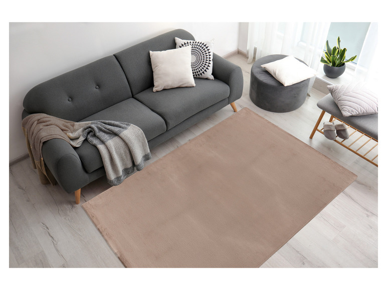 Ein beiger Teppich vor einem grauen Sofa.