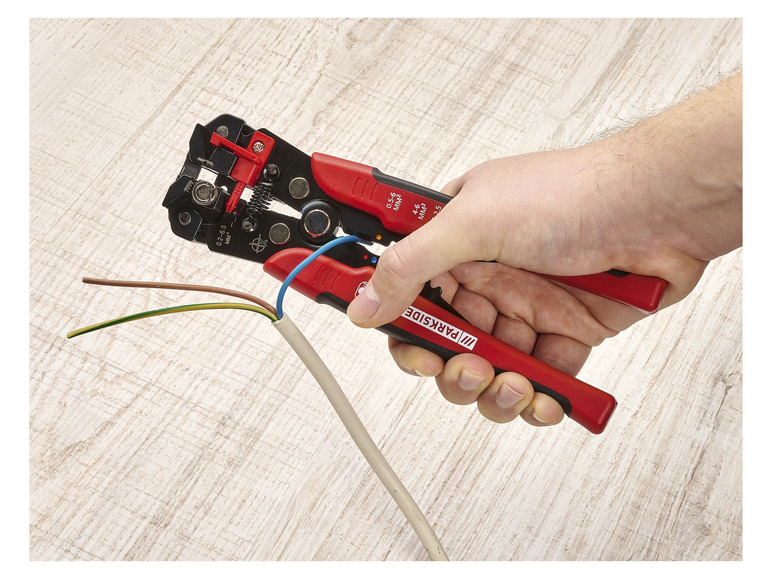 Eine Hand hält eine rote Parkside Drahtabisolierzange mit Drähten.