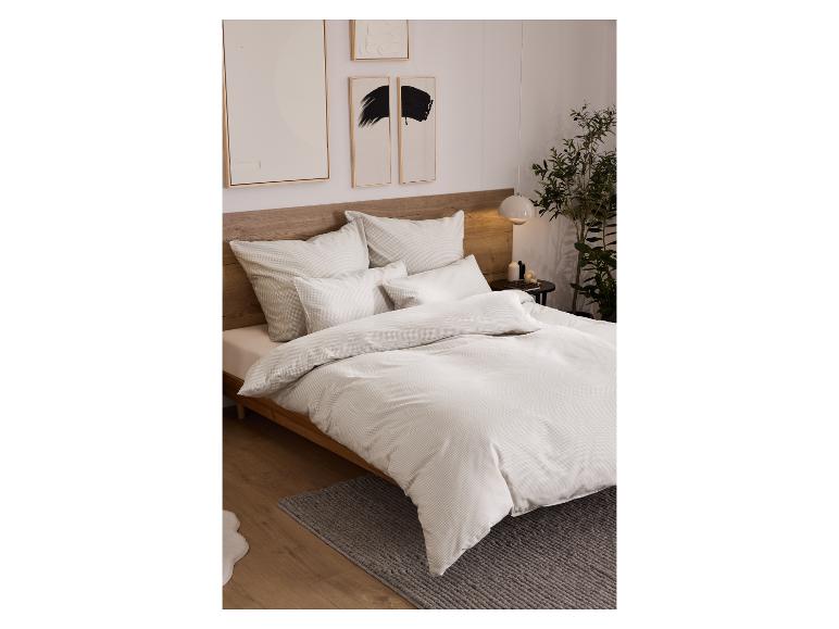 Ein Bett mit weißer Bettwäsche mit dezentem Muster in einem modernen Schlafzimmer.