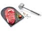 Ein Steak auf einem Marmorbrett mit einem Fleischhammer.