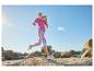 Frau läuft in fuchsiafarbenem T-Shirt und gemusterten Leggings in felsiger Landschaft unter blauem Himmel.