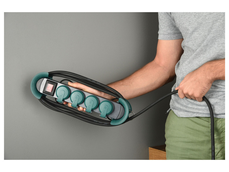 Ein Mann hält eine grüne Steckdosenleiste mit 4 Steckdosen fest.