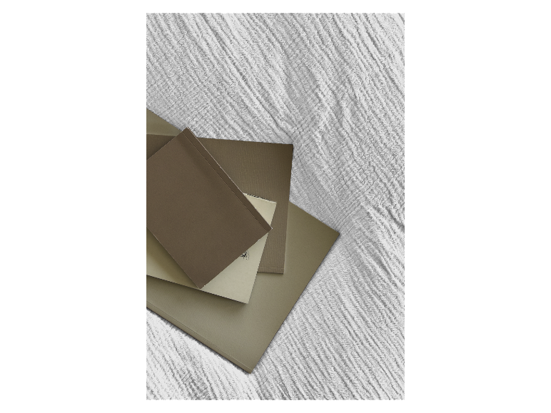 Beige und braune Ordner und Notizbücher auf einem strukturierten Stoff gestapelt.