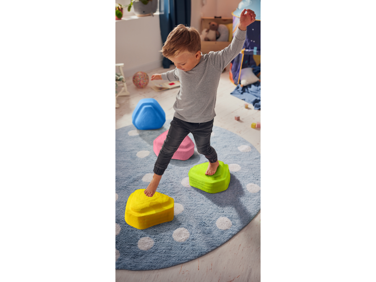Junge balanciert auf bunten Trittsteinen auf einem runden Teppich.