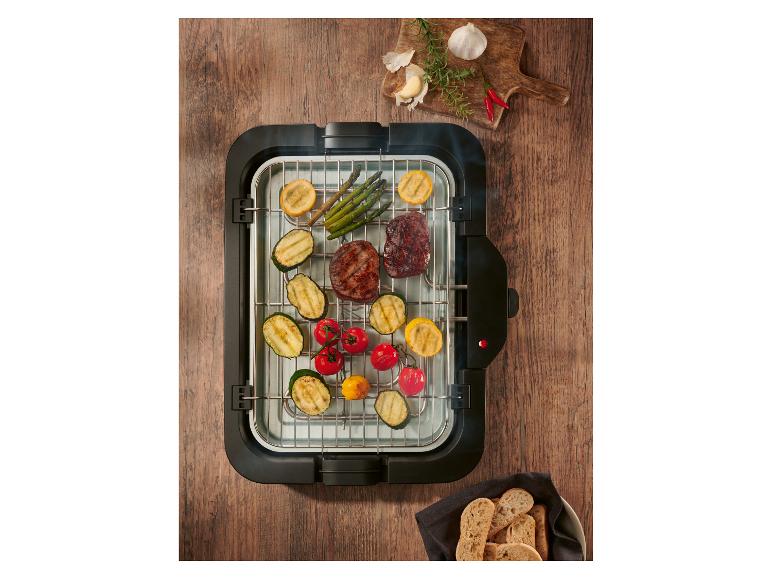 Elektrogrill mit gegrilltem Fleisch und Gemüse, Gewürzen und Brot auf einem Holztisch.