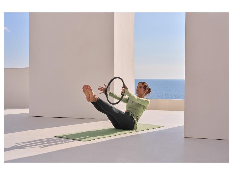 Frau im CRIVIT Funktionstop macht Pilates mit einem Ring auf einer Matte.