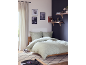 Modernes Schlafzimmer mit Holzbett, Bettwäsche mit Pflanzenmuster, Wandregalen und Teppich.