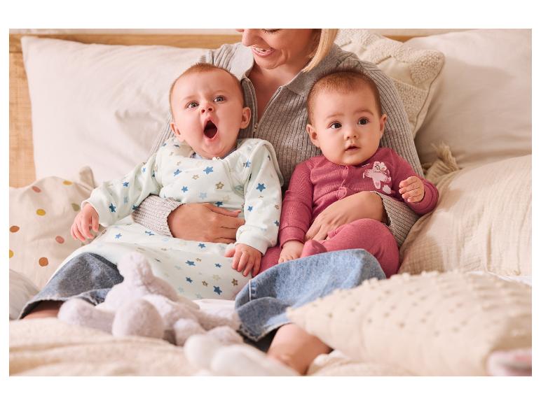 Eine Frau hält zwei Babys in Schlafsäcken auf einem Bett.