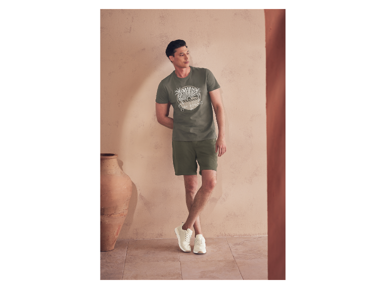 Mann in olivgrünem T-Shirt und Shorts, trägt helle Sneakers.