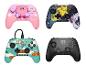 Vier Gamecontroller: rosa mit einer Zeichentrickfigur, schwarz mit Zeichentrickfiguren, blau mit einer Zeichentrickfigur und schwarz.