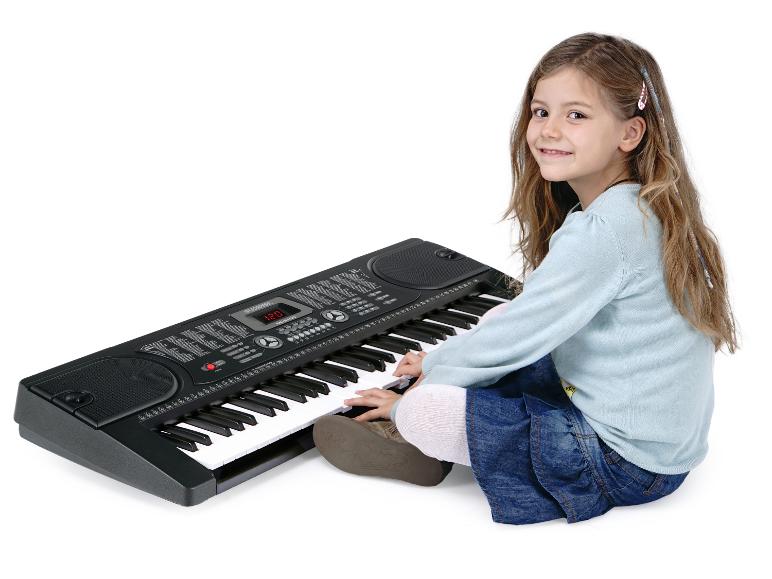 Ein junges Mädchen sitzt auf dem Boden und spielt ein schwarzes elektronisches Keyboard.